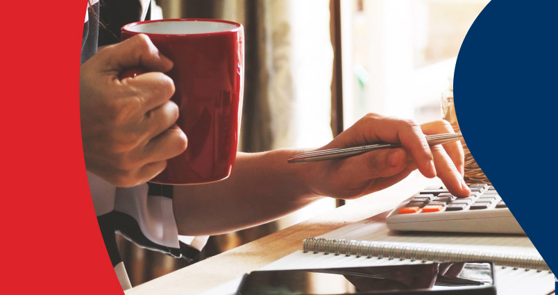 A young man with coffee in hand, submitting his tax returns on his computer.